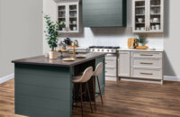 A kitchen with a modern wood hood with shiplap details and a hunter green painted finish surrounded by off-white, light gray cabinets with a dramatic flat panel door style.