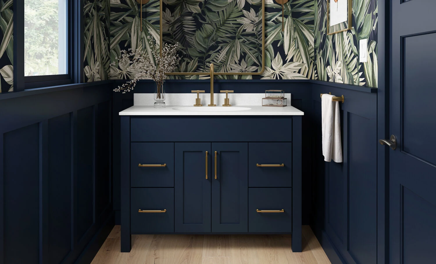 A trendy navy blue bathroom with a furniture style blue vanity with a solid white countertop, gold/brushed brass hardware, blue wainscot panels, and a fashionable blue, green, and white wallpaper.