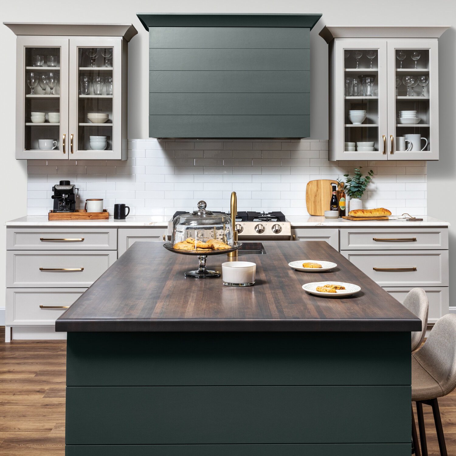 A kitchen with a modern wood hood with shiplap details and a hunter green painted finish surrounded by off-white, light gray cabinets with a dramatic flat panel door style.
