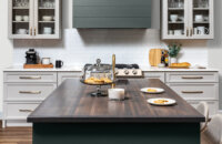 A kitchen with a modern wood hood with shiplap details and a hunter green painted finish surrounded by off-white, light gray cabinets with a dramatic flat panel door style.