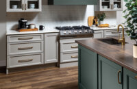 A kitchen with a modern wood hood with shiplap details and a hunter green painted finish surrounded by off-white, light gray cabinets with a dramatic flat panel door style.
