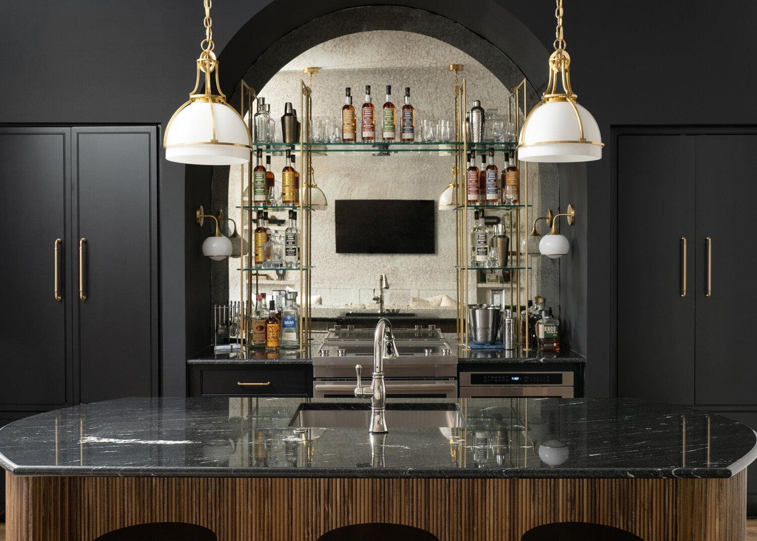 Dark and moody wet bar space in a basement entertainment room featuring black painted cabinets and glass shelving.