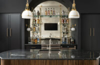 Dark and moody wet bar space in a basement entertainment room featuring black painted cabinets and glass shelving.
