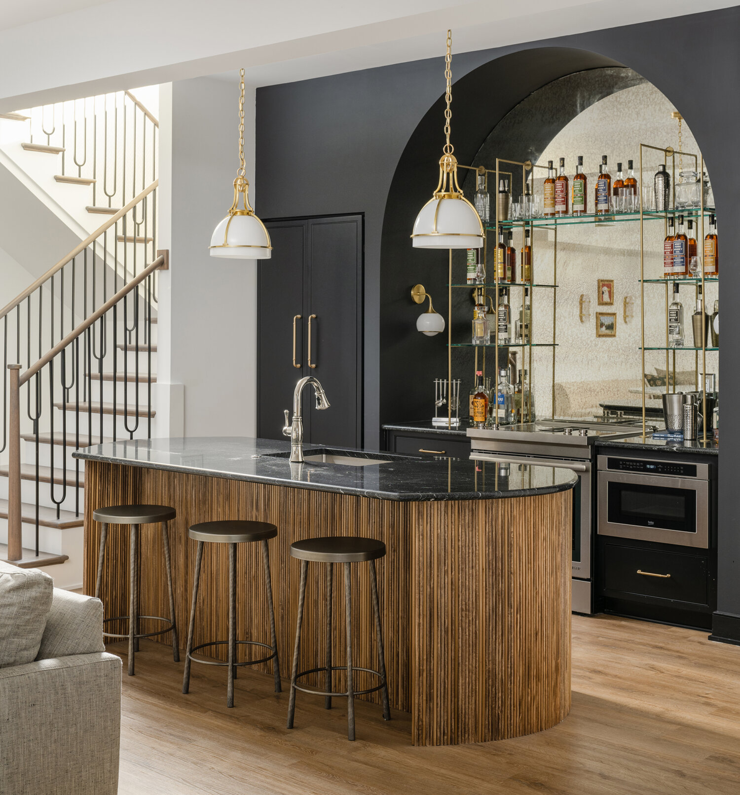 Dark and moody wet bar space in a basement entertainment room featuring black painted cabinets and glass shelving.