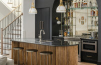 Dark and moody wet bar space in a basement entertainment room featuring black painted cabinets and glass shelving.