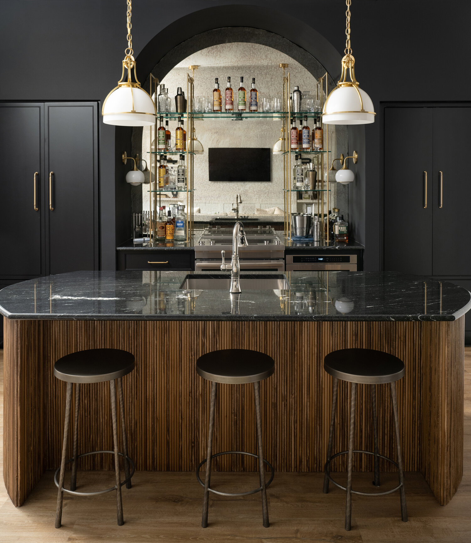 Dark and moody wet bar space in a basement entertainment room featuring black painted cabinets and glass shelving.