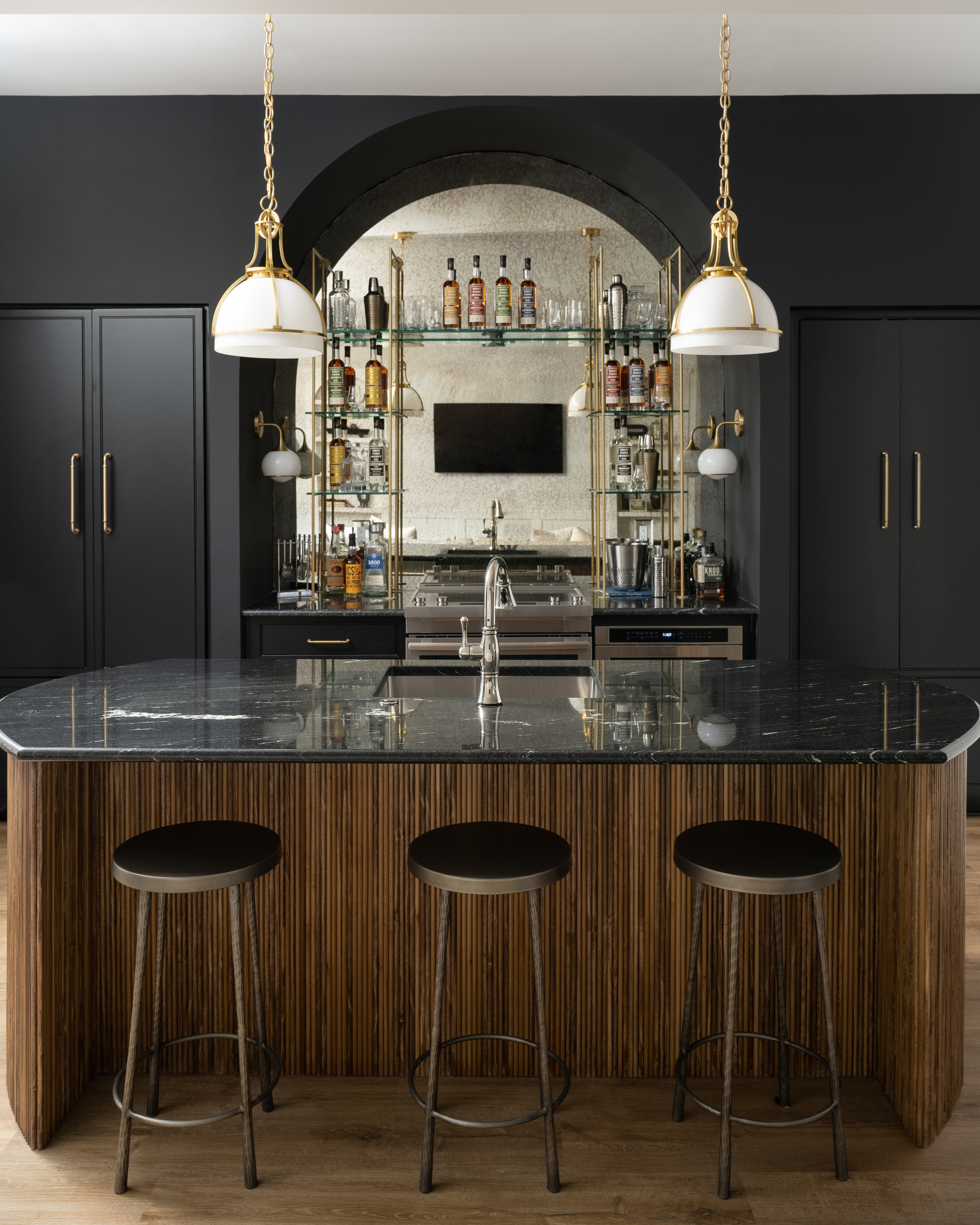 Dark and moody wet bar space in a basement entertainment room featuring black painted cabinets and glass shelving.