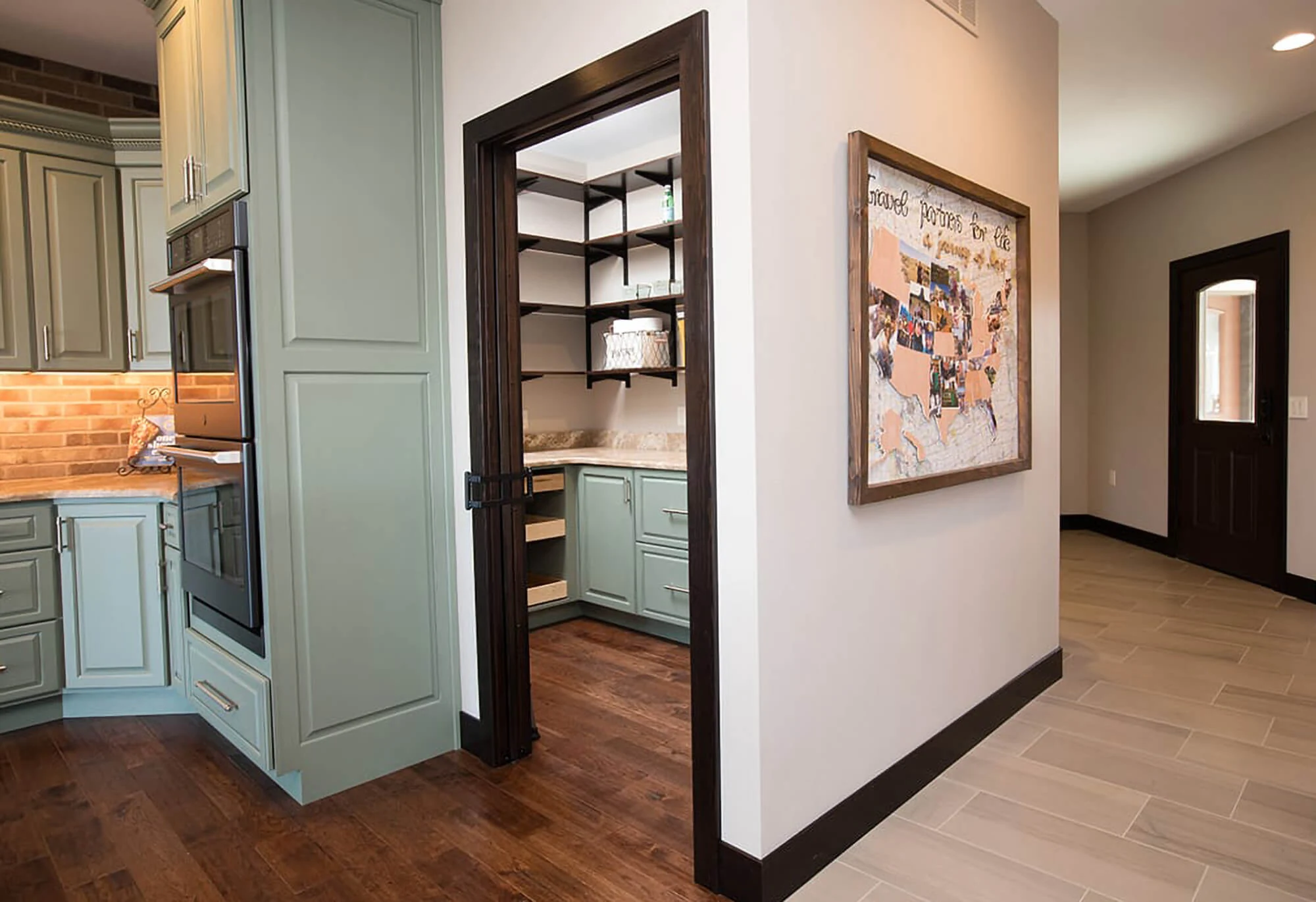 A soft, sage green and dark brown kitchen design with butler's pantry.