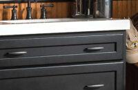 A dresser styled bathroom vanity with a black painted finish and furniture style details.
