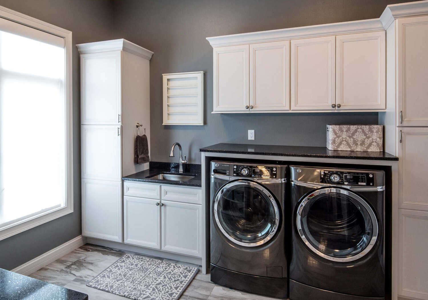 A classic white and gray laundry room with white painted shaker cabinetry.
